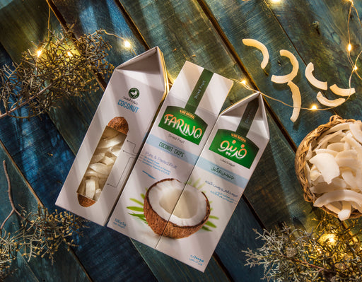 Three packages of coconut chips on a wooden surface with decorative lights and coconuts.