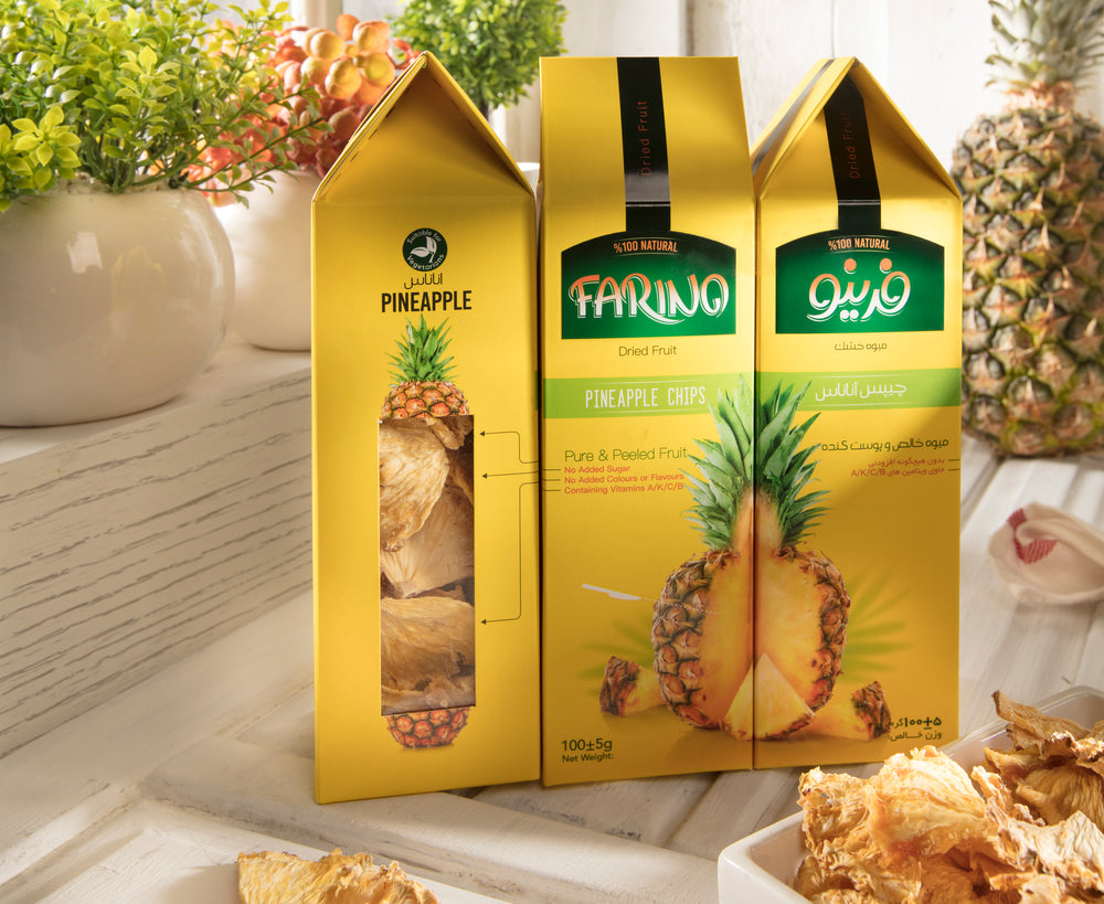 Three boxes of Farino pineapple chips on a table with pineapples and plants in the background.